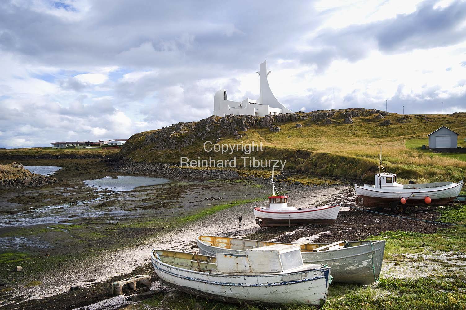 Scenic view at Stykkisholmur, Iceland, with small boats at low tide and the modern white church Stykkishólmskirkja on a rocky hill, designed by Jon Haraldsson 